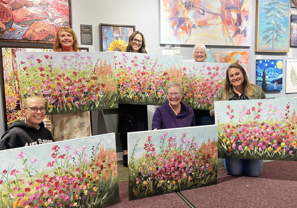 group of women in art gallery holding up flower painting
