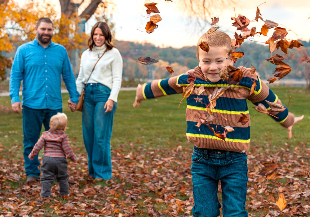 young family playing in the leaves in a park