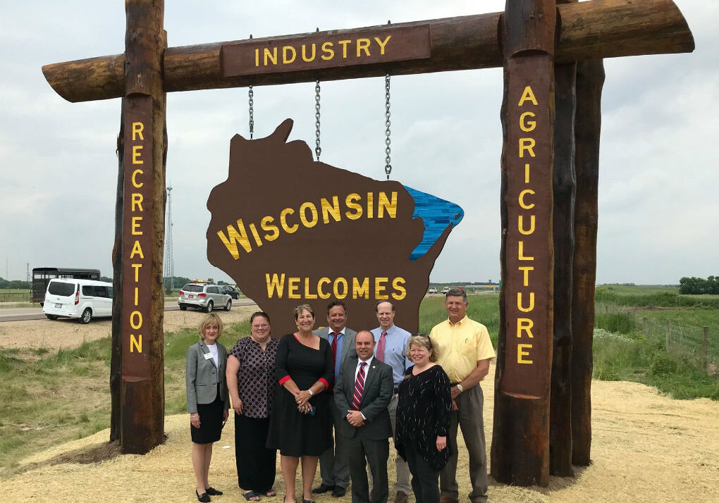 group of people standing in front of wisconsin welcomes you sign on highway