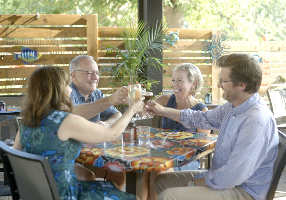 Four people cheering drinks at a patio table.