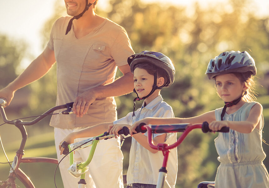 Happy family is riding bikes outdoors, looking forward and smiling