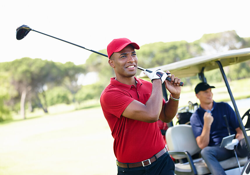 Shot of a young man taking a shot while his friend congratulates him from the golf cart in the background