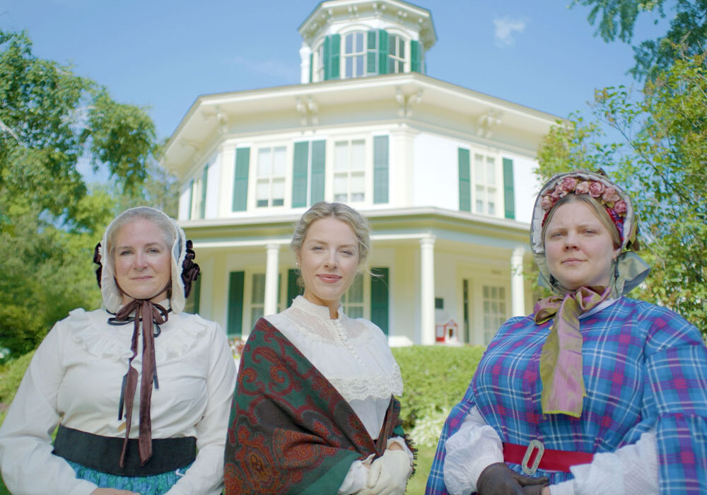 octagon-house-hudson-wi three women dressed up in period costumes in front of historic octagon house