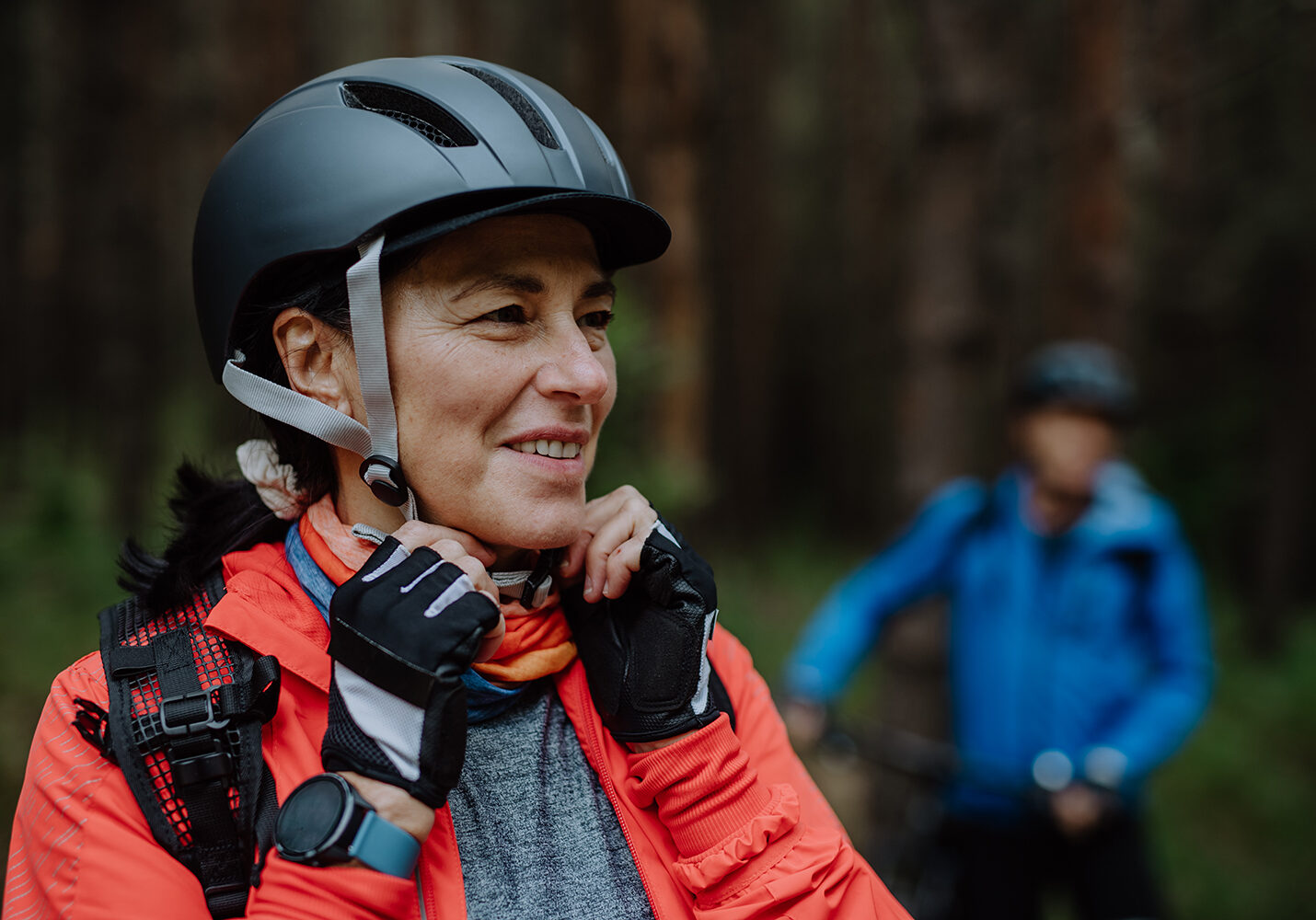 Senior woman biker putting on cycling helmet outdoors in forest in autumn day. A senior woman biker putting on cycling helmet outdoors in forest in autumn day.