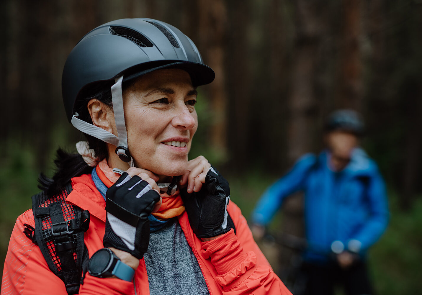 A senior woman biker putting on cycling helmet outdoors in forest in autumn day.